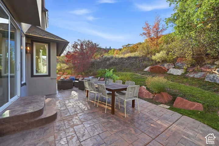 Expansive stamped concrete patio with curved steps, featuring a built-in outdoor light fixture, and a sloped, landscaped yard with mature plantings and natural rock elements
