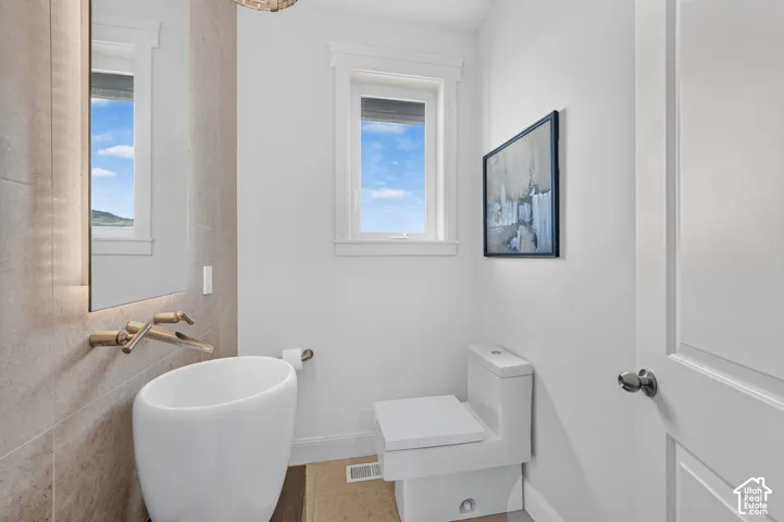 White pedestal sink, wall-mounted faucet, full-height tile, and window with natural light