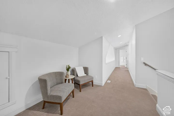 Carpeted corridor with sloped walls, white painted walls, and recessed lighting