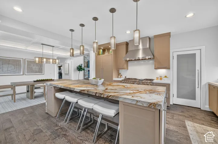 Gourmet kitchen with a large island featuring a stone countertop, wood-finish flooring, a stainless steel range hood, and custom cabinetry