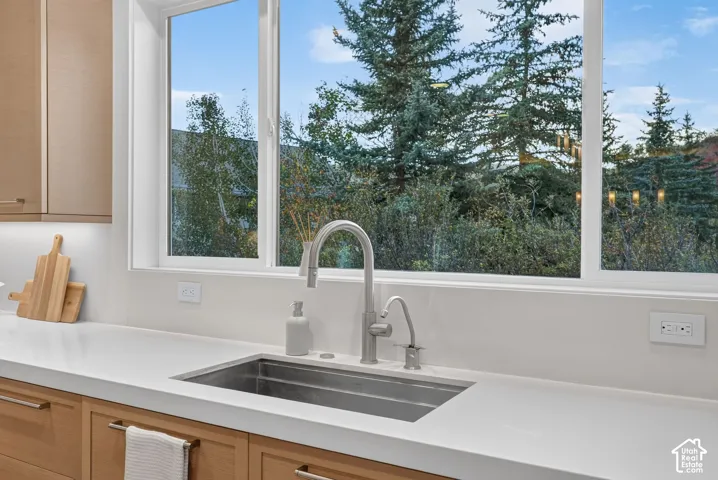 Stainless steel undermount sink with a brushed nickel faucet, light wood-finish cabinetry, and white countertops