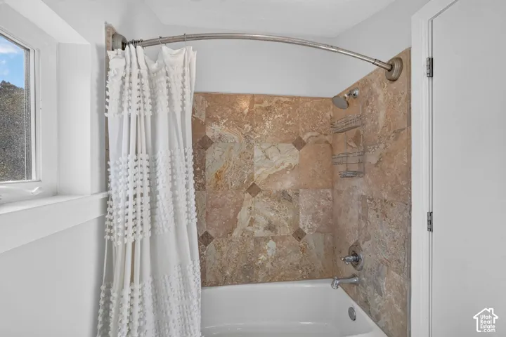 Bathtub with a natural stone tile surround featuring decorative inserts, and a chrome shower fixture