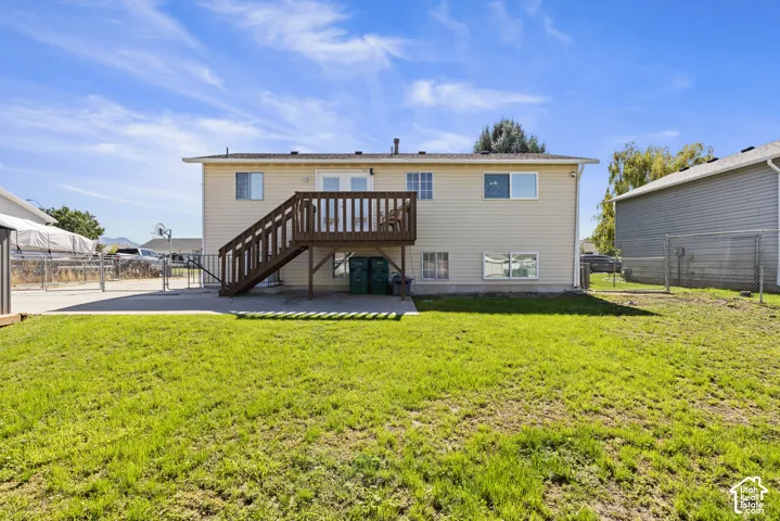 Expansive backyard featuring a concrete patio, wood-finish deck, and chain-link fence