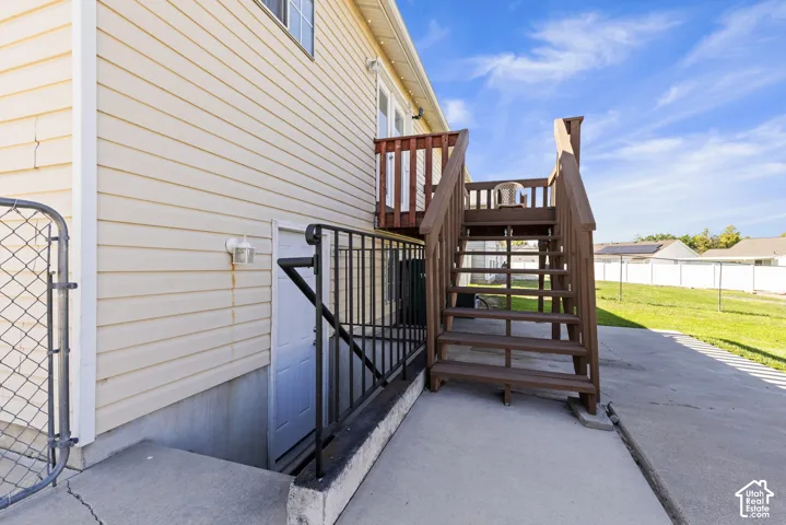 Exterior featuring beige horizontal siding, a wooden deck with railing, concrete patio, and a chain link gate