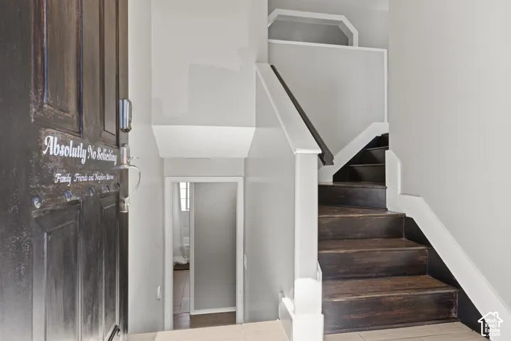 Wood-finish entry door with dark hardware, a light-toned flooring, and a staircase featuring dark wood-finish treads and white risers