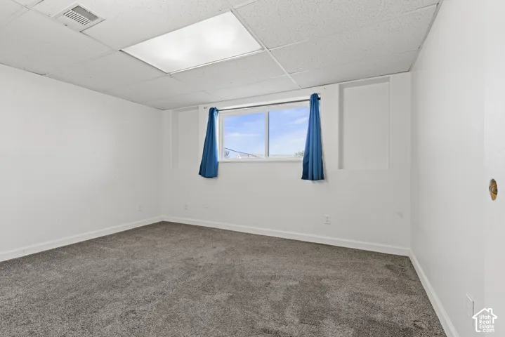 Wall-to-wall carpeting, white painted walls, drop ceiling, recessed lighting, and a window with natural light