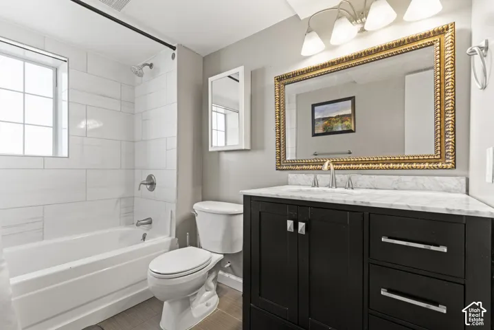 Bathroom featuring a dark wood vanity with a light-toned countertop, a large ornate framed mirror, and a tiled shower-tub combination with a window