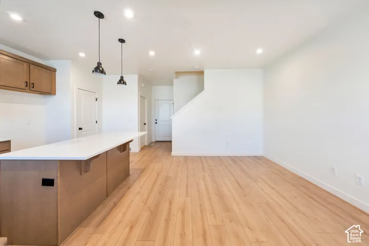 Kitchen island with a white countertop, wood-finish flooring, recessed lighting, and pendant light fixtures