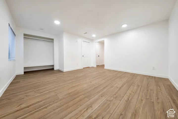 Spacious room featuring wood-finish flooring, recessed lighting, and a built-in closet with shelving and hanging rod