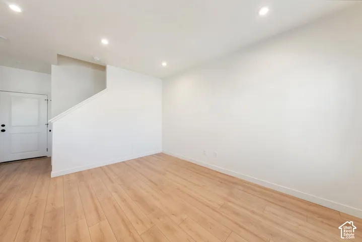 Recessed lighting illuminates the open living space with wood-finish flooring and a white paneled door