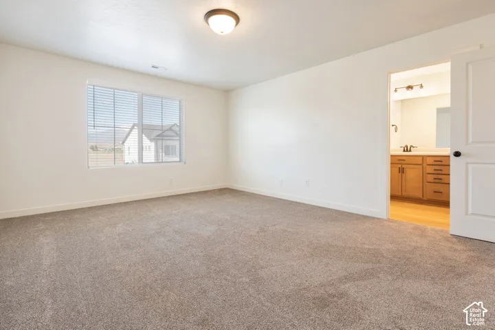 Spacious room featuring neutral carpeting, a large window with blinds, and a flush-mount ceiling light