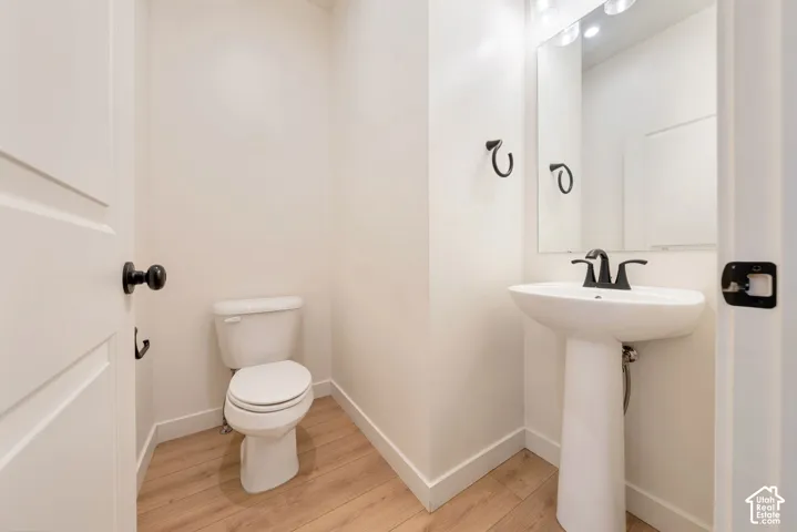 Pedestal sink with a matte black faucet, wall-mounted mirror, and wood-finish flooring