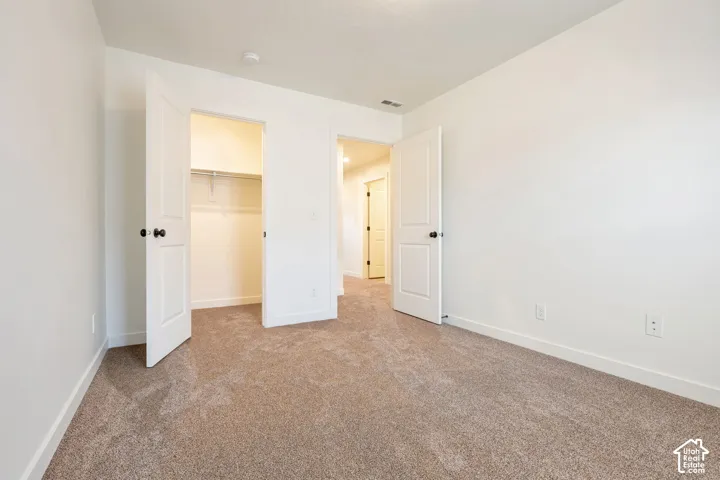 Neutral tone wall finish, plush carpet flooring, white paneled doors, and a built-in closet with shelving and hanging rods