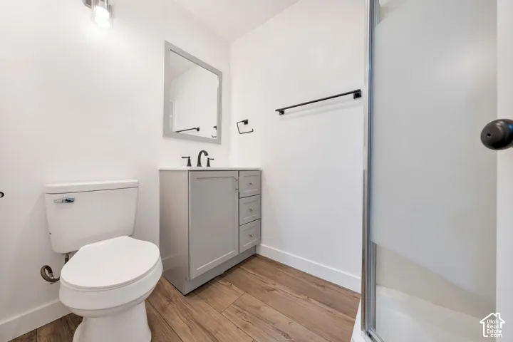 White walls, wood-finish flooring, gray vanity with storage, matte black hardware, and an enclosed shower