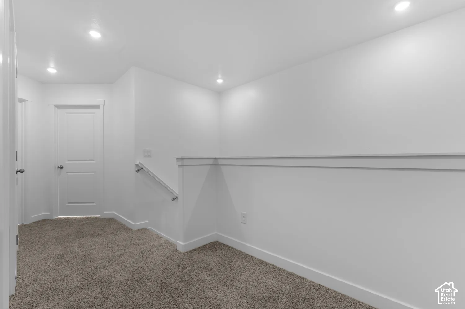 Recessed lighting, neutral carpeting, crisp white walls, and a white two-panel door