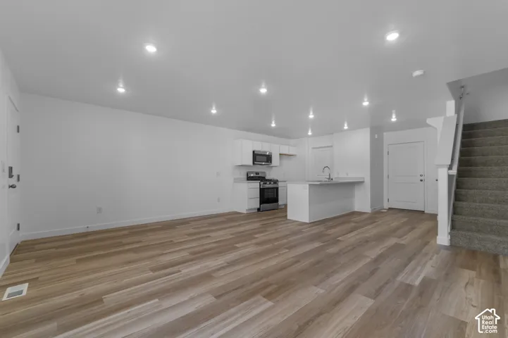 Open concept living space featuring wood-finish flooring, recessed lighting, and a modern kitchen with white cabinetry