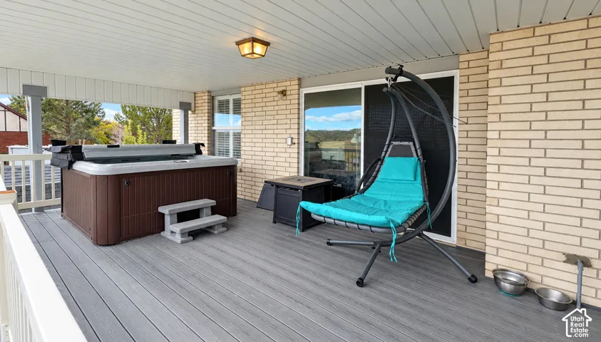 Covered deck with composite flooring, recessed ceiling, integrated hot tub, and brick exterior wall