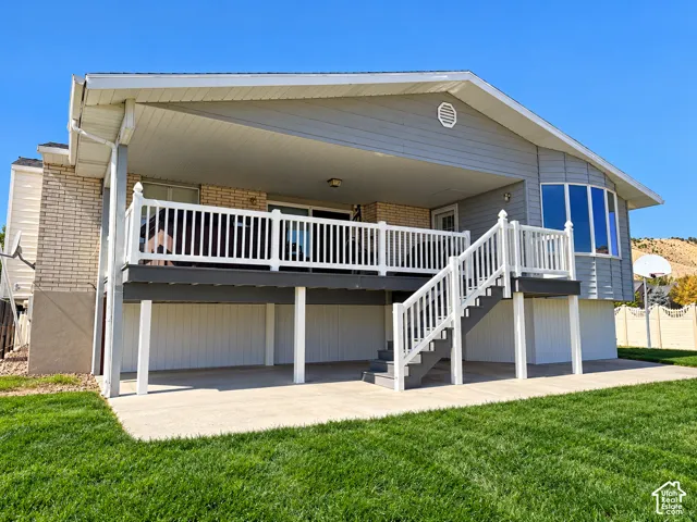 Expansive deck with white railing, covered patio area, concrete hardscaping, and a bay window