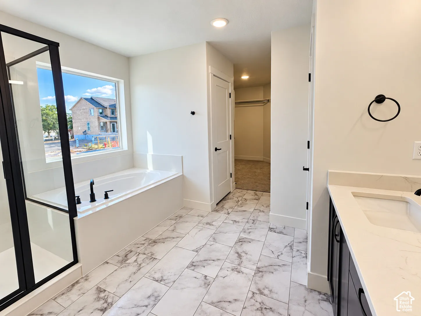 Contemporary bathroom with marble-finish tile flooring, a built-in soaking tub, and a shower with a black-framed glass enclosure