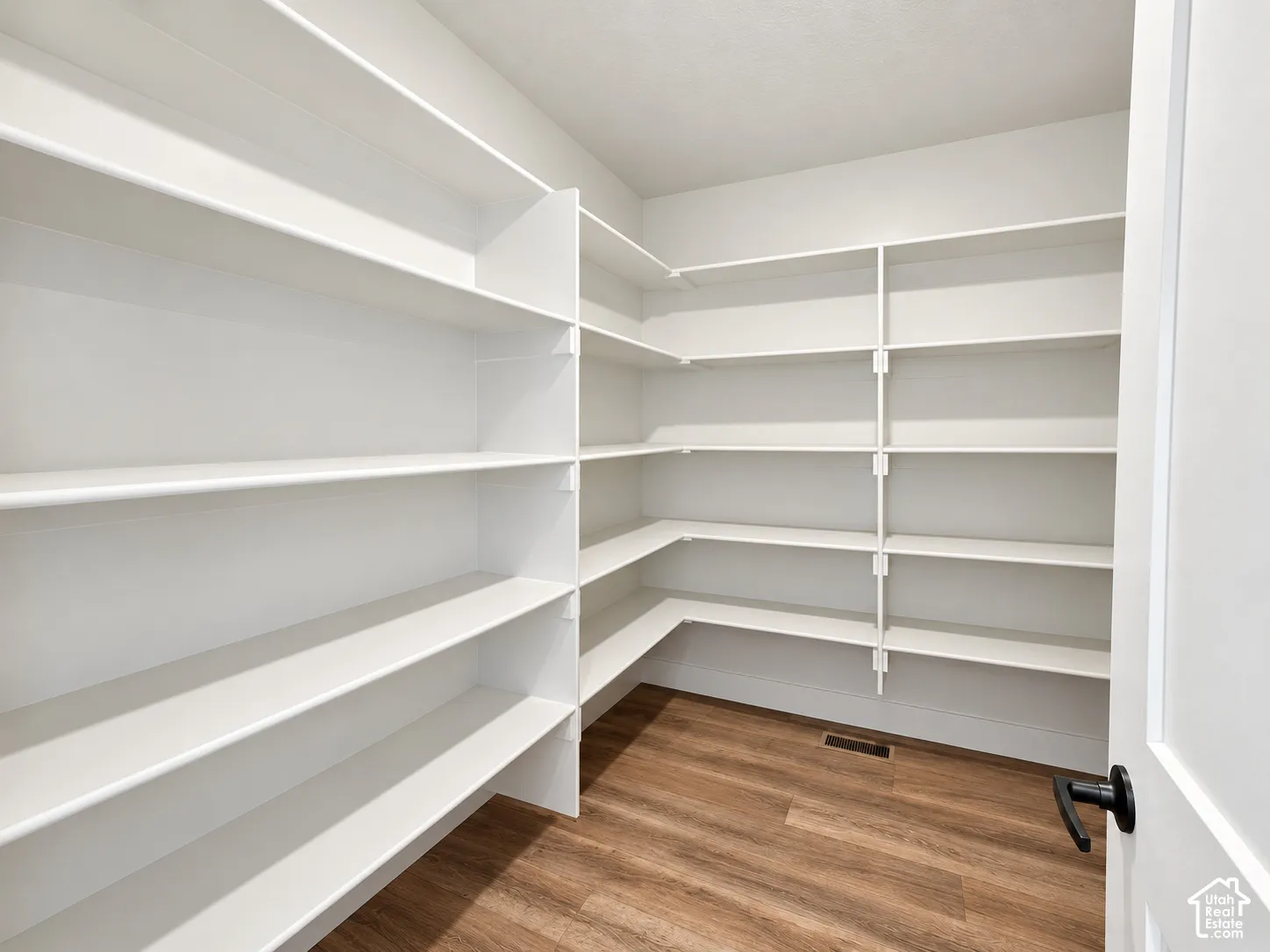 Expansive pantry featuring extensive white shelving, wood-finish flooring, and white trim