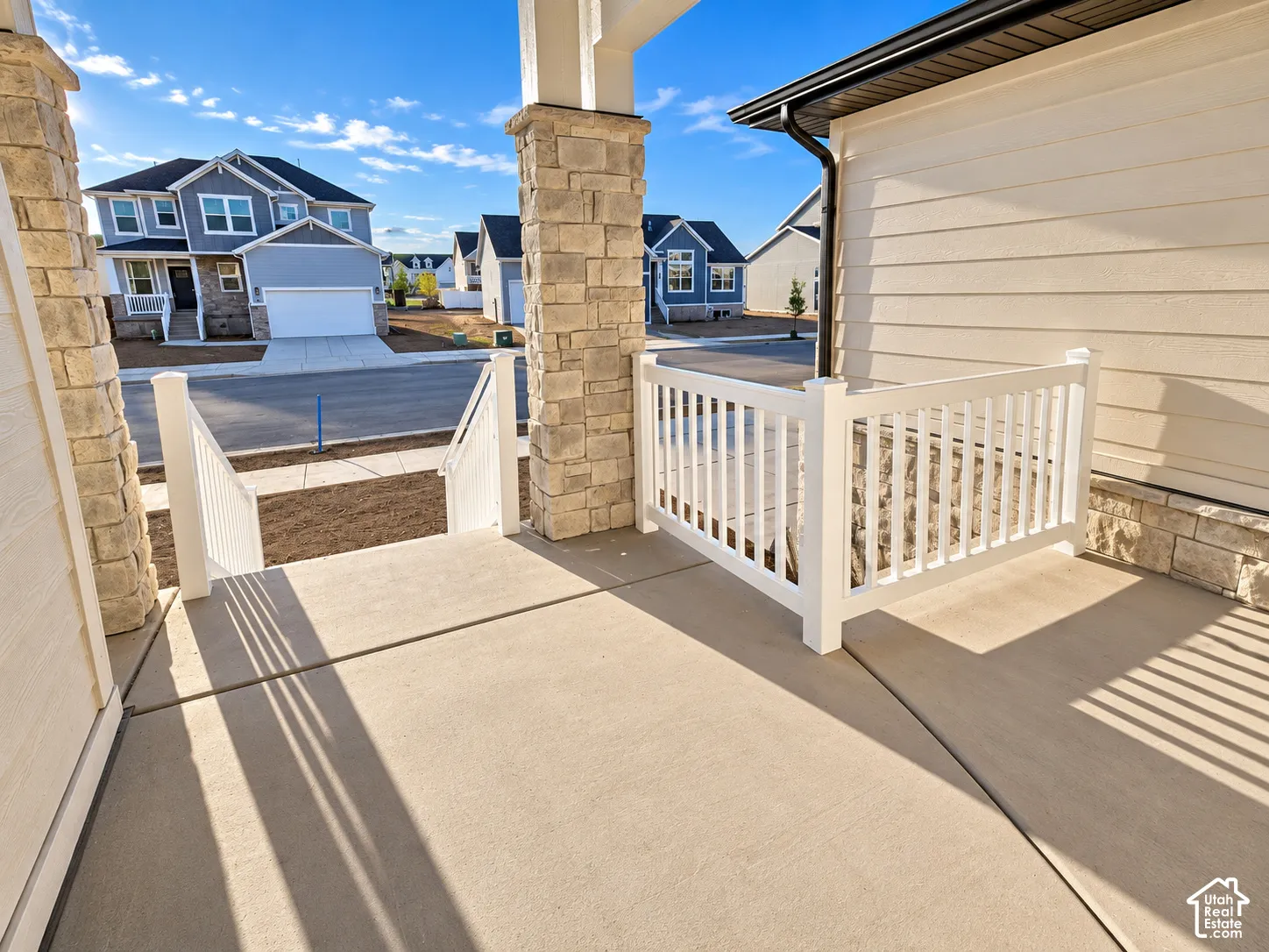 Front porch featuring stone-clad columns, durable concrete flooring, and white railing
