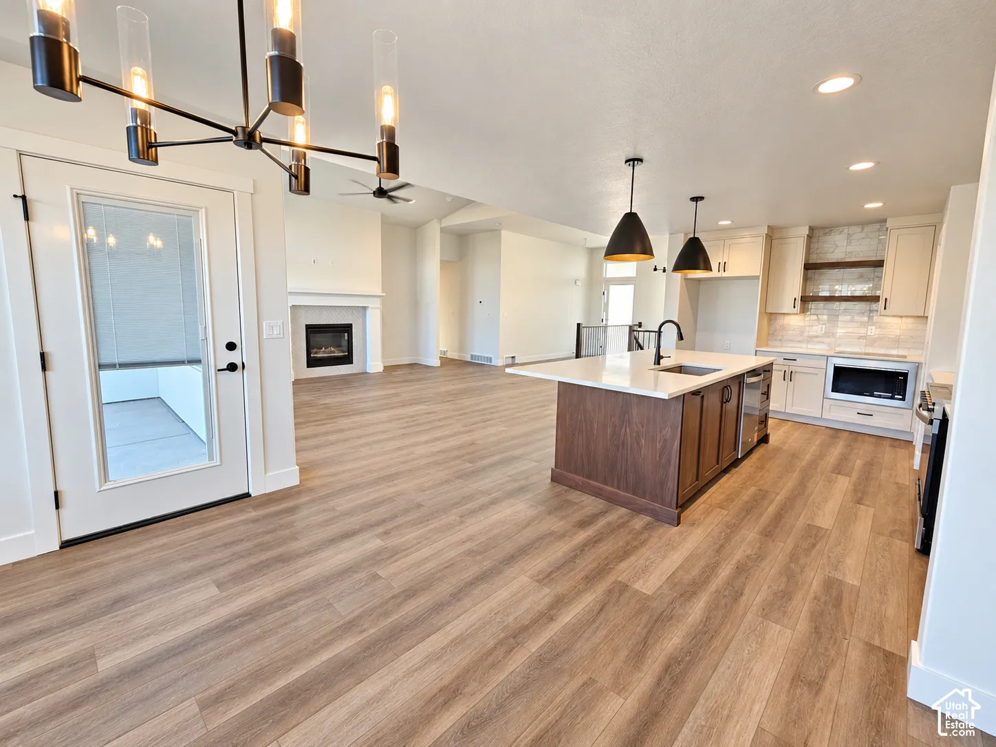 Open-concept living space with wood-finish flooring, a contemporary kitchen island with a white countertop, recessed lighting, a built-in fireplace, and a modern chandelier