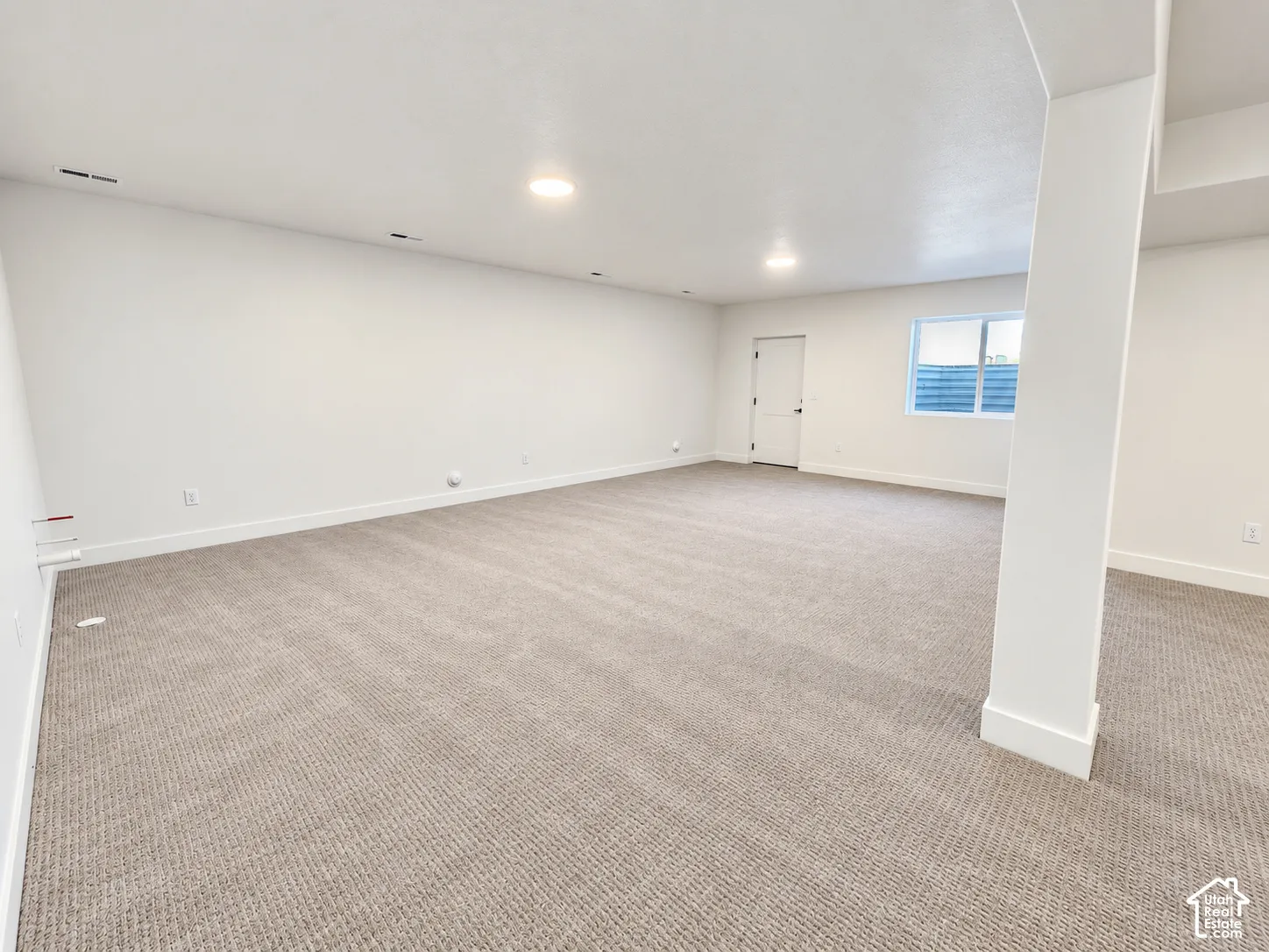 Spacious room featuring neutral carpeting, recessed lighting, white walls, a permanent support column, and a window providing natural light