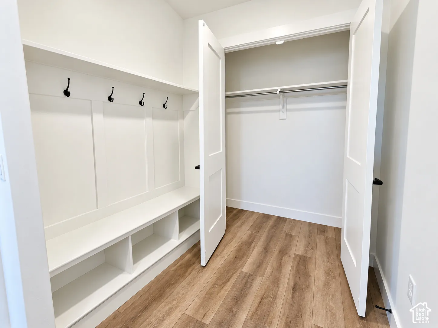 Built-in bench seating with storage, wall-mounted coat hooks, wood-finish flooring, and double-door closet with hanging rod