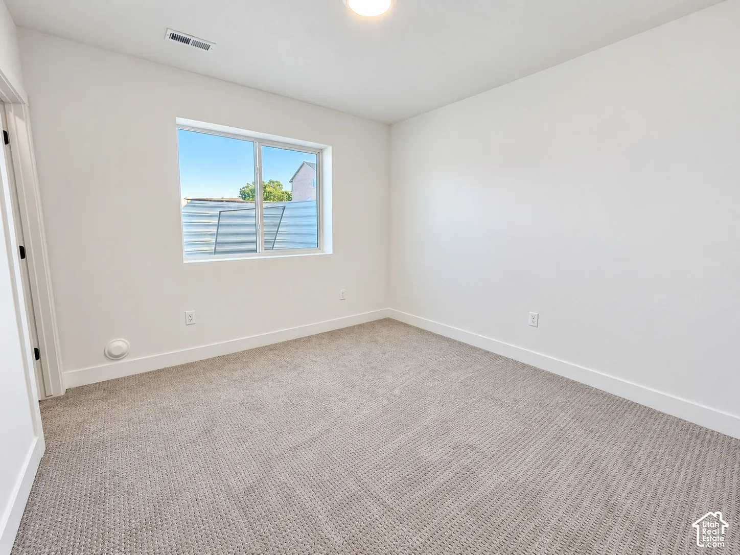 Neutral paint palette, recessed ceiling light, white trim, light-toned carpet, and a window with a window well