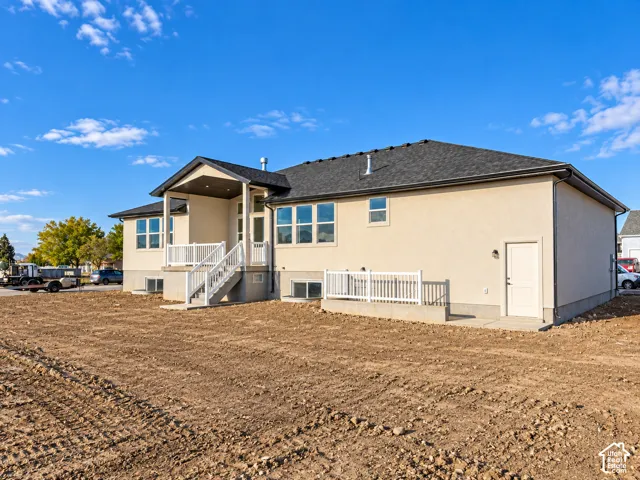 Rear exterior featuring a covered patio, white railing, multiple windows, and a lower-level access door