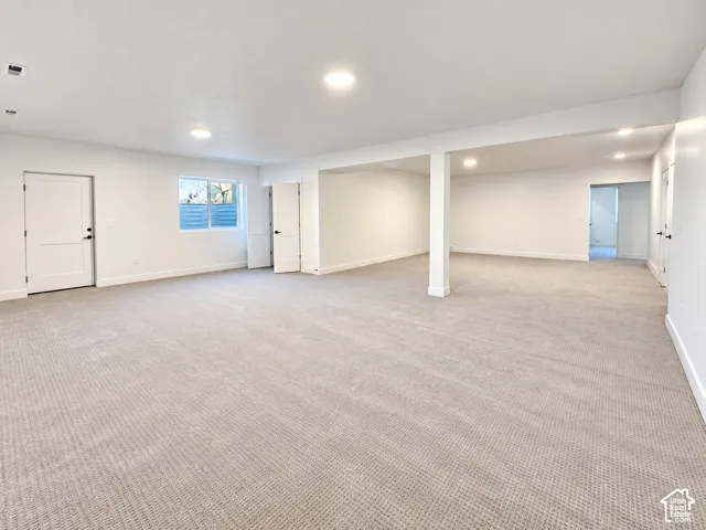 Expansive carpeted area with recessed lighting, multiple white doors, and a window with horizontal blinds