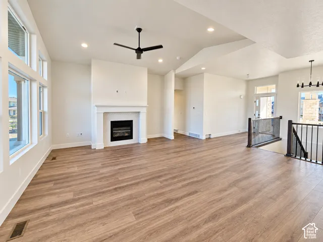 Spacious room featuring wood-finish flooring, a contemporary fireplace with a white mantel and tile surround, multiple large windows, and a modern ceiling fan