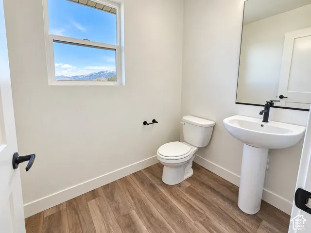 Pedestal sink with a matte black faucet, wall-mounted mirror, wood-finish flooring, and white baseboards