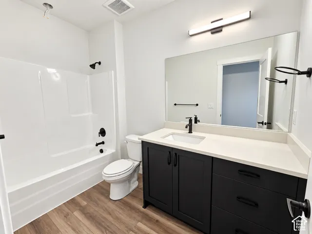 Wood-finish flooring, black shaker-style vanity, light-toned countertop, black fixtures, and a white integrated tub/shower unit
