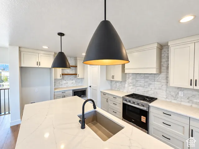 Expansive kitchen island with an undermount sink and matte black faucet, light-toned cabinetry, stainless steel range, and a full-height marble-look tile backsplash