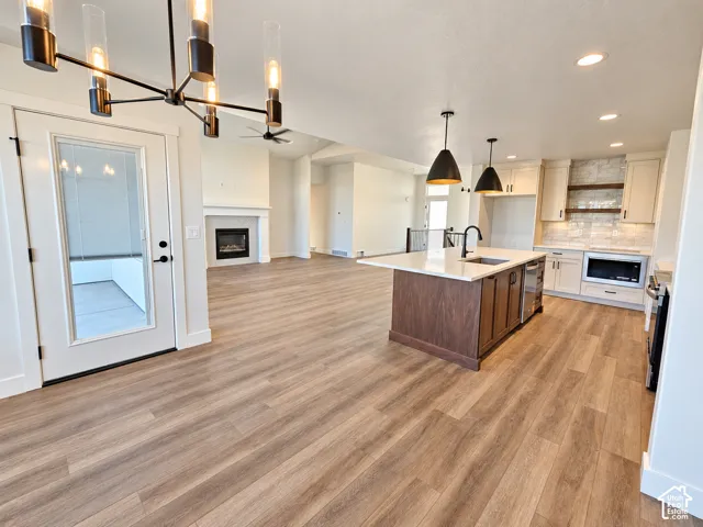 Open-concept living space with wood-finish flooring, a contemporary kitchen island with a white countertop, recessed lighting, a built-in fireplace, and a modern chandelier