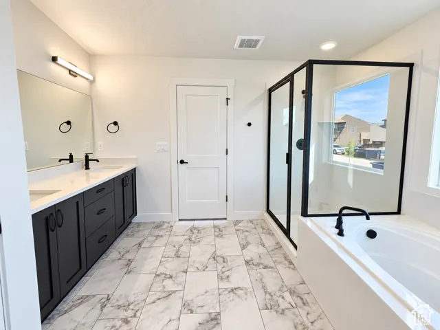Spacious bathroom featuring a dual vanity with dark cabinetry, a built-in soaking tub, a separate glass-enclosed shower, and light-toned tile flooring