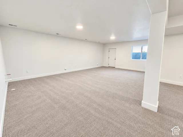 Spacious room featuring neutral carpeting, recessed lighting, white walls, a permanent support column, and a window providing natural light