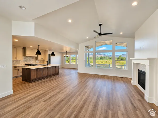 Vaulted ceilings, wood-finish flooring, a kitchen island with built-in cabinetry, an integrated fireplace, and expansive windows