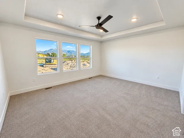 Recessed ceiling with integrated lighting, contemporary ceiling fan, three expansive windows, neutral wall tones, and textured carpeting