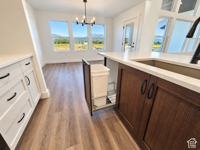 Wood-finish flooring throughout, white cabinetry with black hardware, dark wood-finish island cabinetry, white countertops, and a black chandelier