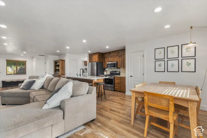 Open-concept living area with wood-finish flooring, a kitchen featuring wood cabinetry and stainless steel appliances, a kitchen island with seating, and recessed lighting throughout
