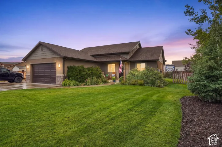 Single-story residence featuring a two-car garage, stone veneer accents, and a front lawn with established landscaping