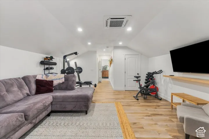 Vaulted white ceilings, recessed lighting, wood-finish flooring, and white walls