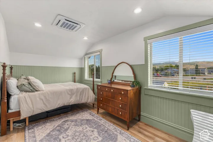 Sloped ceiling room featuring wood-finish flooring, two windows with blinds, recessed lighting, and beadboard wall paneling