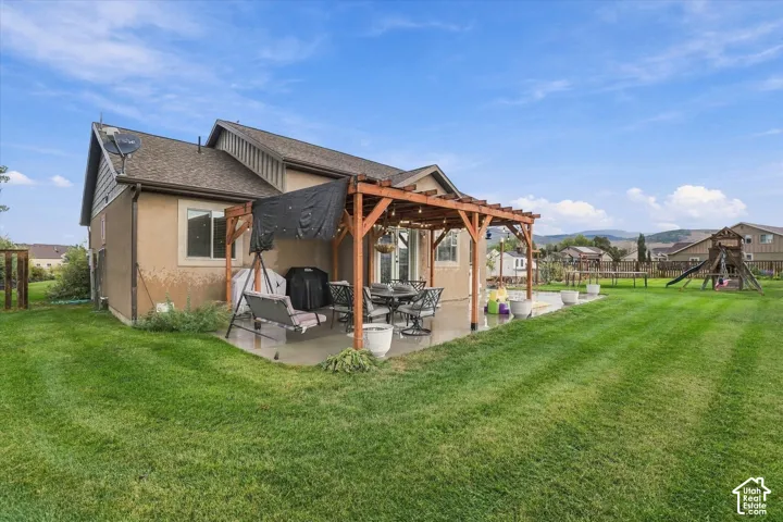 Expansive lawn with a concrete patio, wood pergola, and a large playset