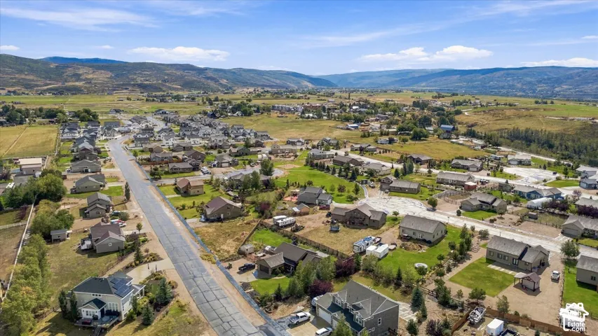 Residential neighborhood with paved roadways and varied home styles, surrounded by expansive green fields and distant mountains