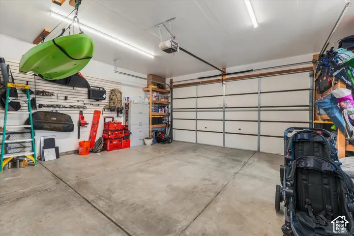 Concrete flooring, overhead strip lighting, sectional garage door, wall-mounted storage panels, and built-in shelving
