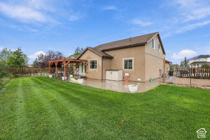 Expansive backyard featuring a manicured lawn, concrete patio, and a wood pergola