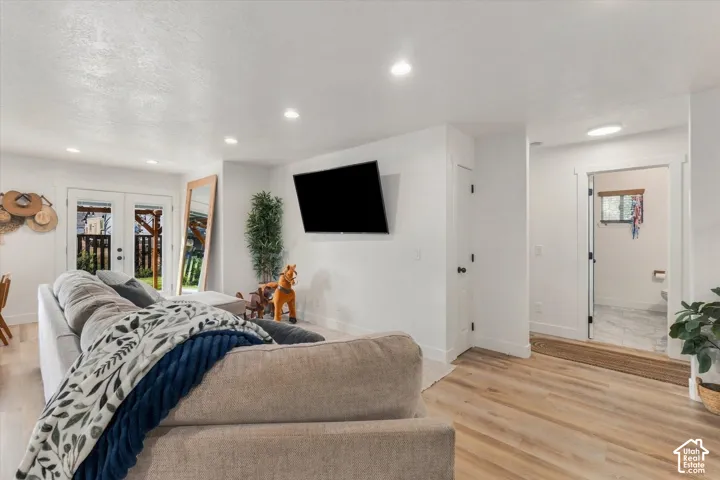 Recessed lighting, light wood-finish flooring, white walls, and double French doors to outdoor decking